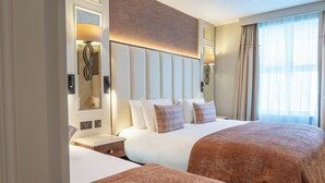 Una habitación de hotel con una cama grande, mesitas de noche, cabecero y una ventana con cortinas.