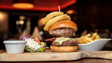 Una hamburguesa con aros de cebolla, una porción de papas fritas y una ensalada pequeña sobre una tabla de madera.