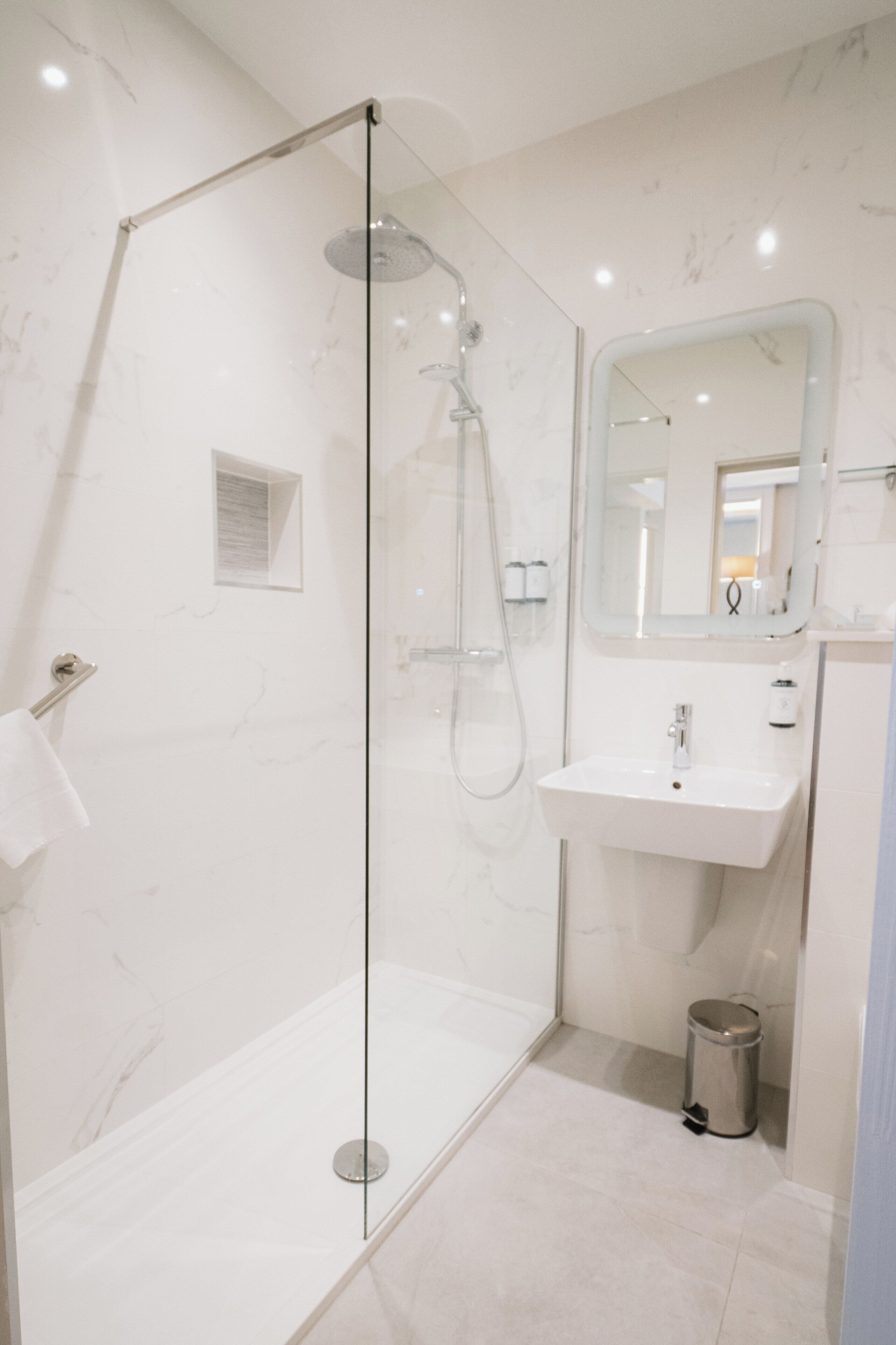 Un baño moderno con ducha de vidrio, lavamanos blanco y espejo sobre el lavamanos.