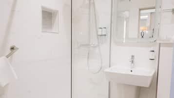 Un baño moderno con ducha de vidrio, lavamanos blanco y espejo sobre el lavamanos.