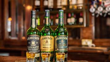 Tres botellas de Jameson Irish Whiskey sobre una superficie de madera, con copas para shots al frente.