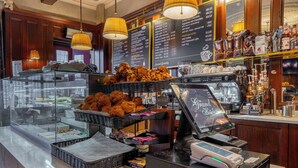 Mostrador de una panadería con una variedad de pasteles, un menú de café y una caja registradora.