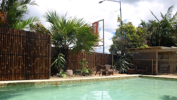 Piscina con cerramiento de bambú, palmeras y mobiliario exterior.