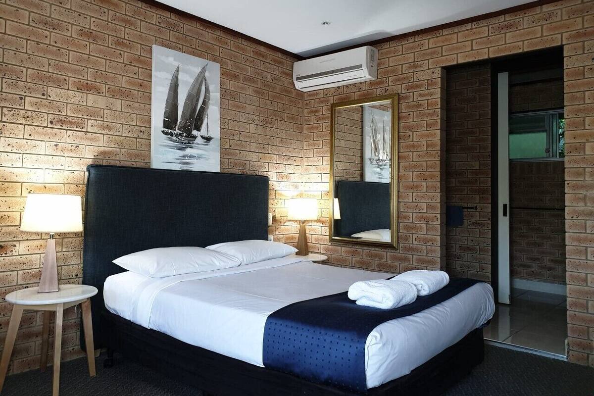 A hotel room with a brick wall, a large bed with white linens, two bedside lamps, and a mirror.