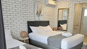 Habitación de hotel con dos camas, ventilador de techo, espejo y pared con diseño de ladrillos.