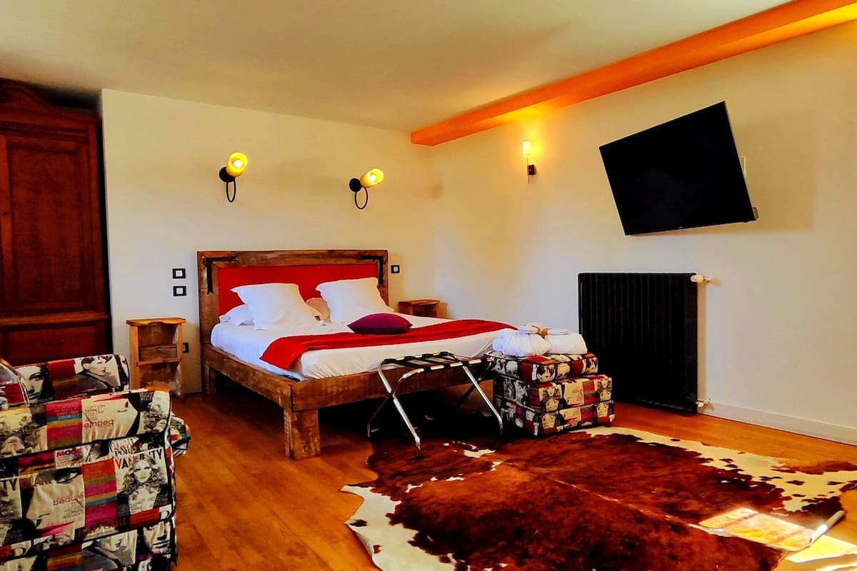 Un dormitorio con una cama de madera, un tapete de cuero de vaca, un escritorio con silla y un televisor montado en la pared.