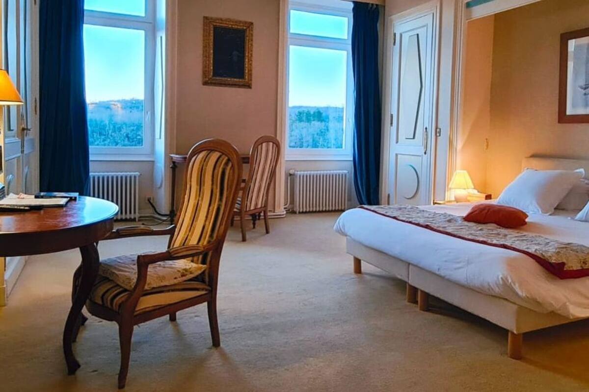 Habitación de hotel con cama, escritorio, dos sillas y vistas al exterior a través de amplias ventanas.