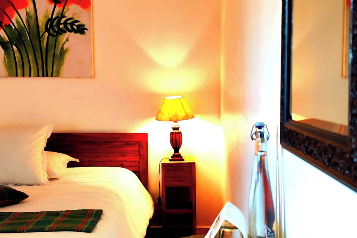 Habitación de hotel con una cama, una lámpara de noche, una botella y un cuadro en la pared.