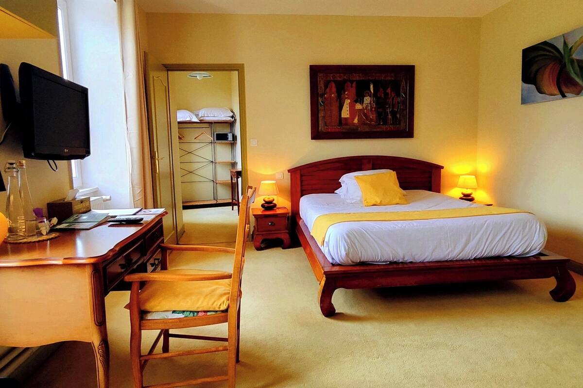 Habitación de hotel con cama, lámparas de noche, un escritorio con silla, televisor y un cuadro en la pared.