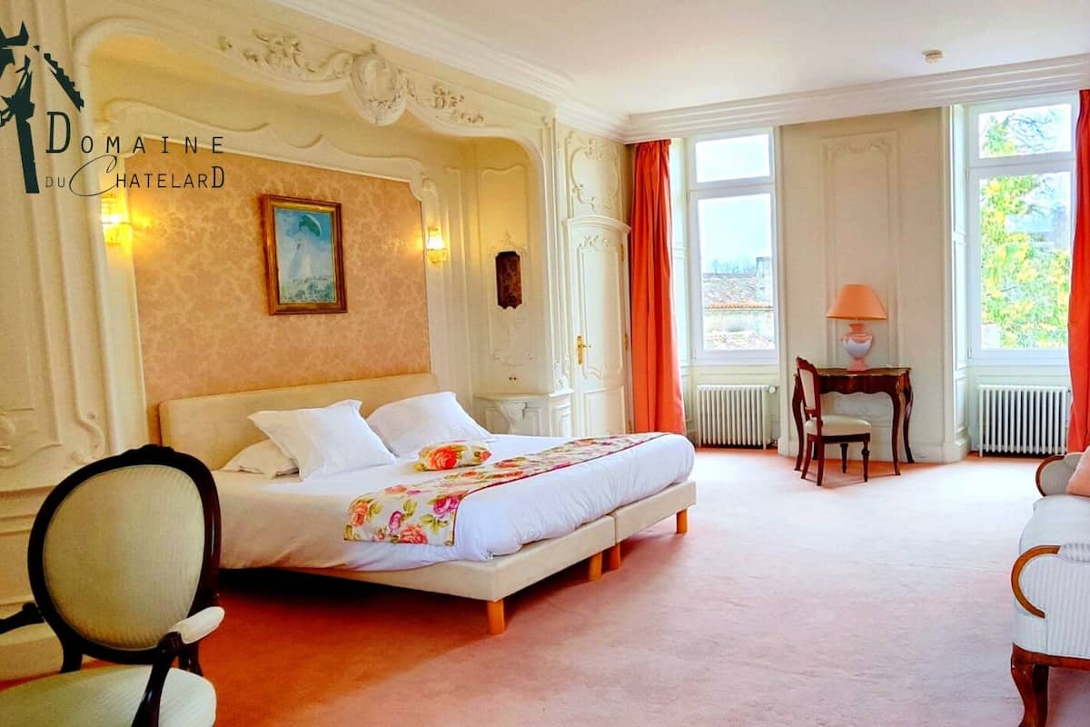 Una habitación de hotel con una cama grande, una silla, una mesita y una ventana con cortinas.