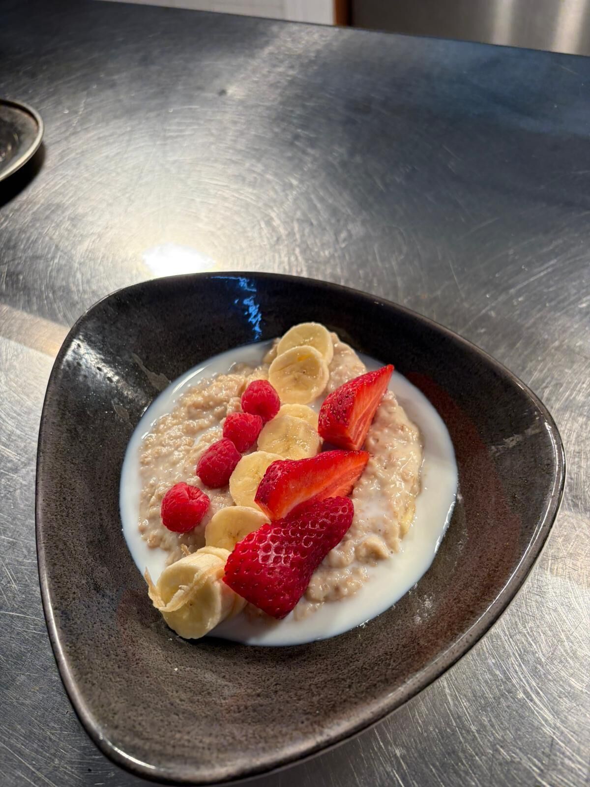 Eine Schüssel Haferflocken mit Erdbeeren und Himbeeren auf einem dunklen Teller.