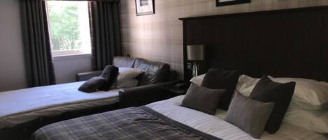 Habitación de hotel con dos camas, un sofá, una lámpara y una ventana con cortinas.
