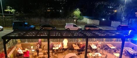 An outdoor patio area with tables and chairs, surrounded by potted plants and a tent.