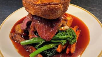 A plate of food with a Yorkshire pudding, beef, vegetables, and sauce.