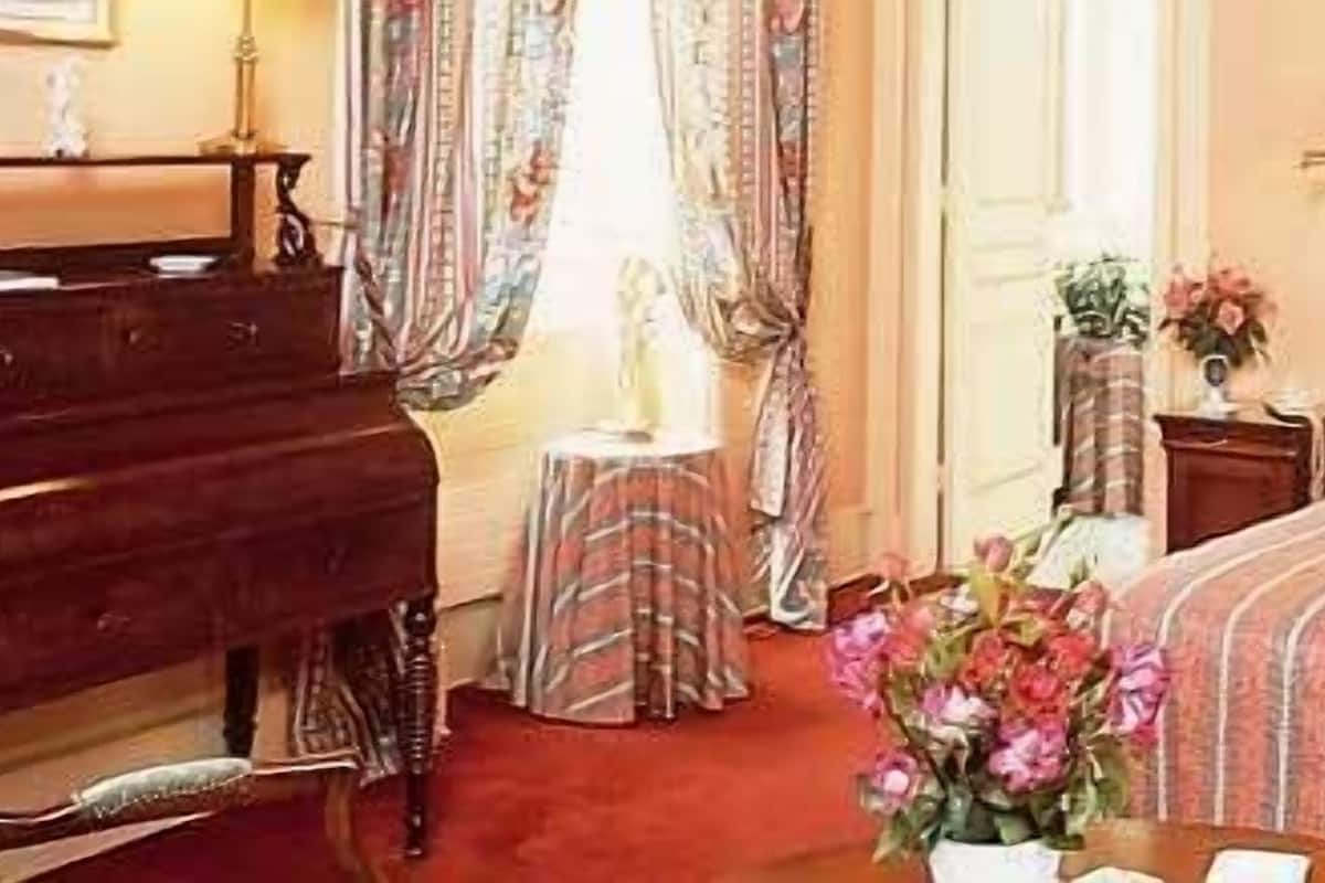 Ein Hotelzimmer mit zwei Betten, einem Schreibtisch, einer Kommode und einem Blumenstrauß.