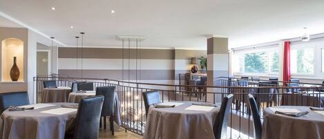 Un comedor con mesas dispuestas para los invitados, una cocina al fondo y vistas al exterior a través de grandes ventanales.
