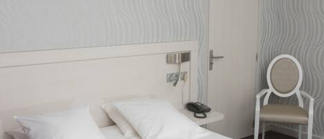 Una habitación de hotel con cama, mesita de noche con teléfono, silla y puerta.