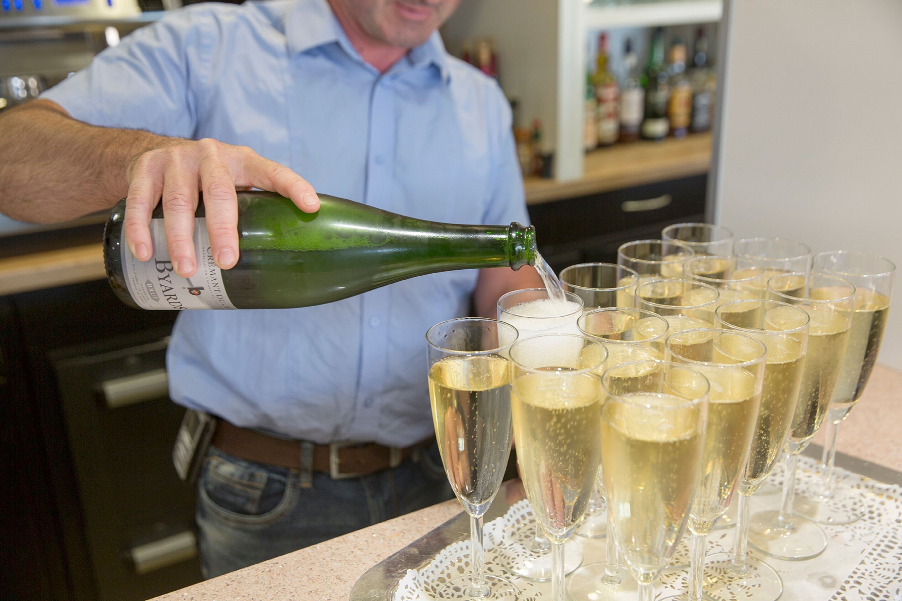 A person pouring champagne into several glasses on a tray.