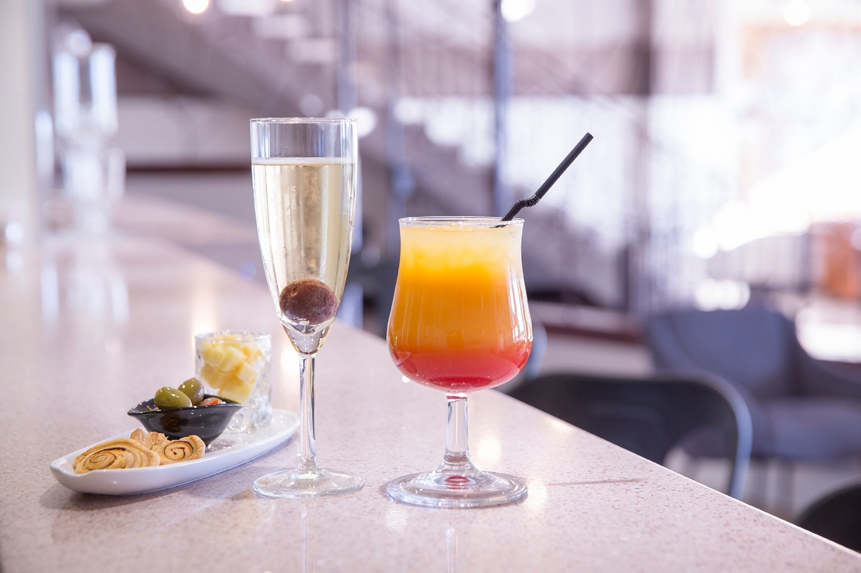 Two drinks on a bar counter, one with a straw and the other with a layered appearance.