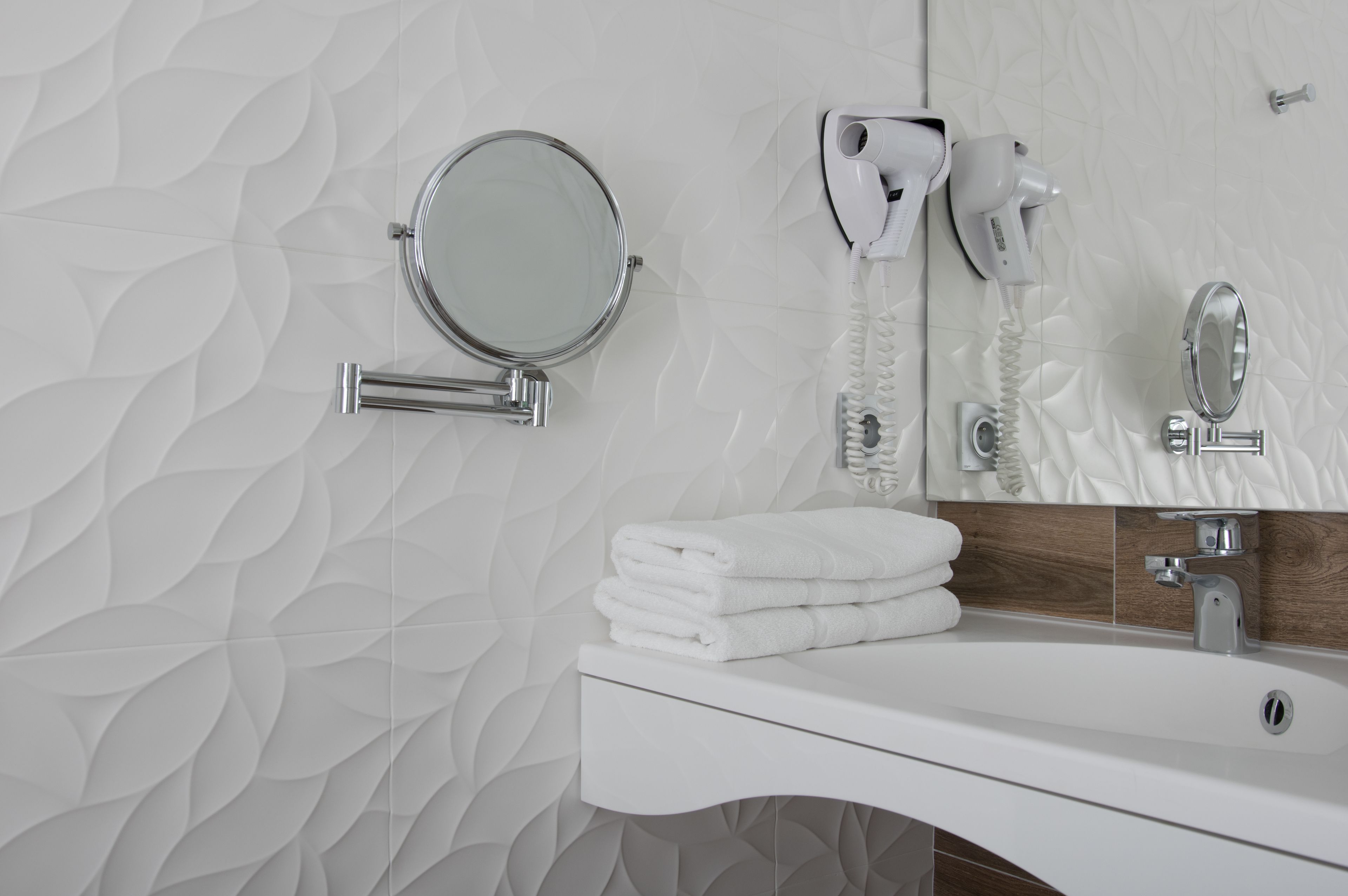 A bathroom with a white sink, a round mirror, a hairdryer, and a towel stack.