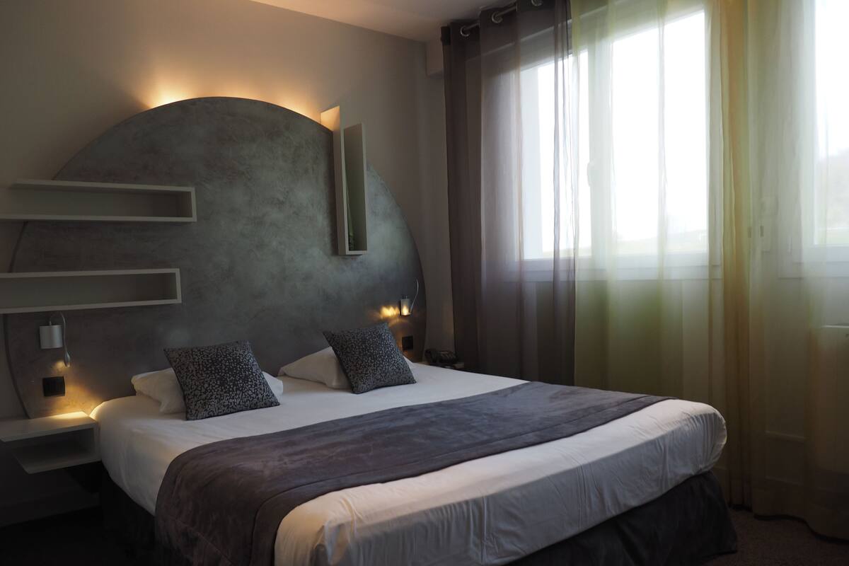 A modern hotel room with a large bed, a curved headboard, and a bedside table with a lamp.