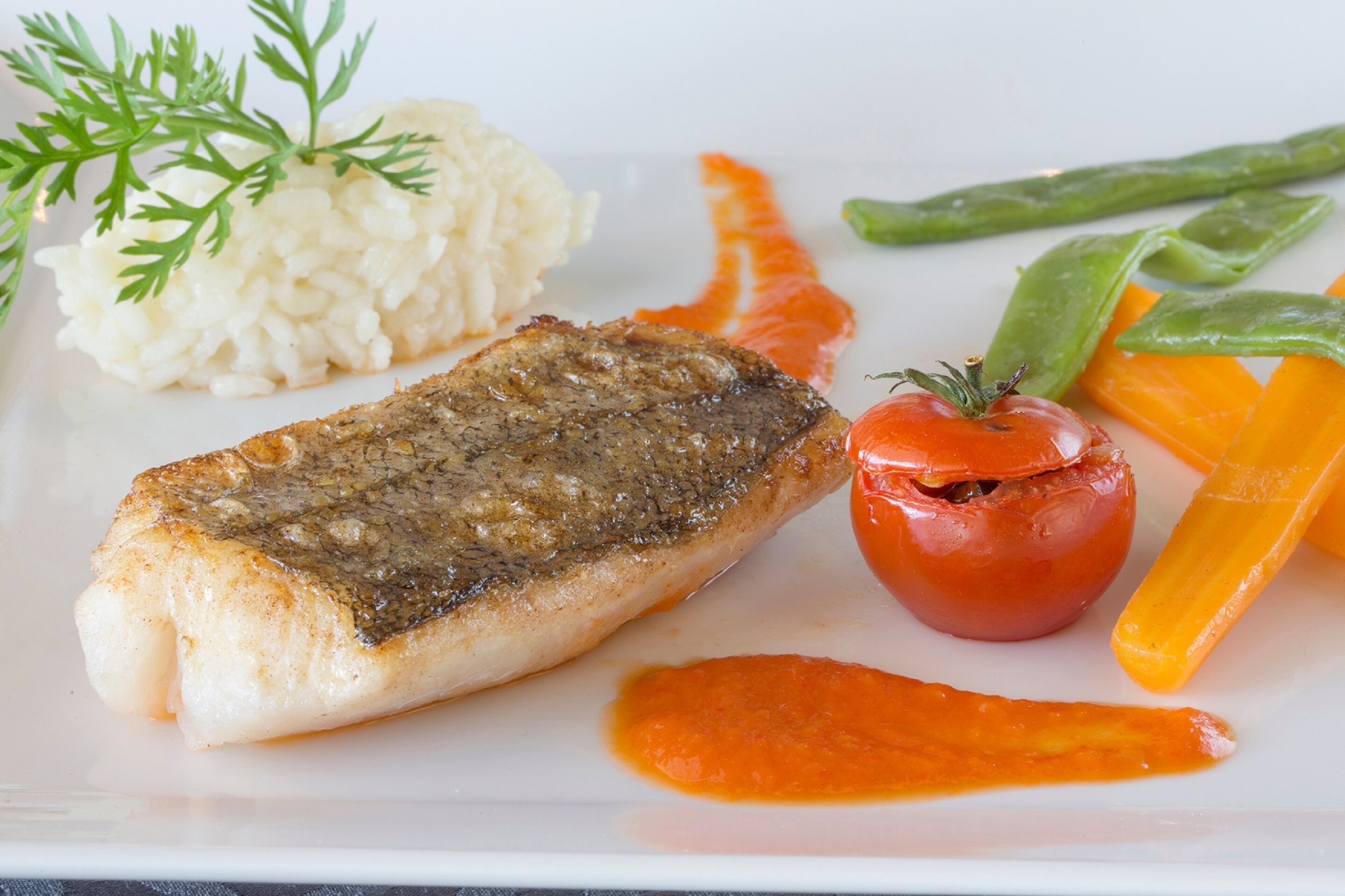 Un plato con un trozo de pescado a la parrilla, arroz blanco, medio tomate y algunos ejotes.