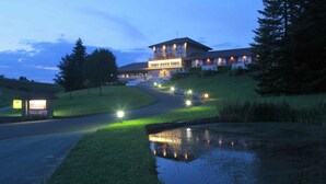 A large, multi-story building with a well-lit entrance and a small pond in the foreground.