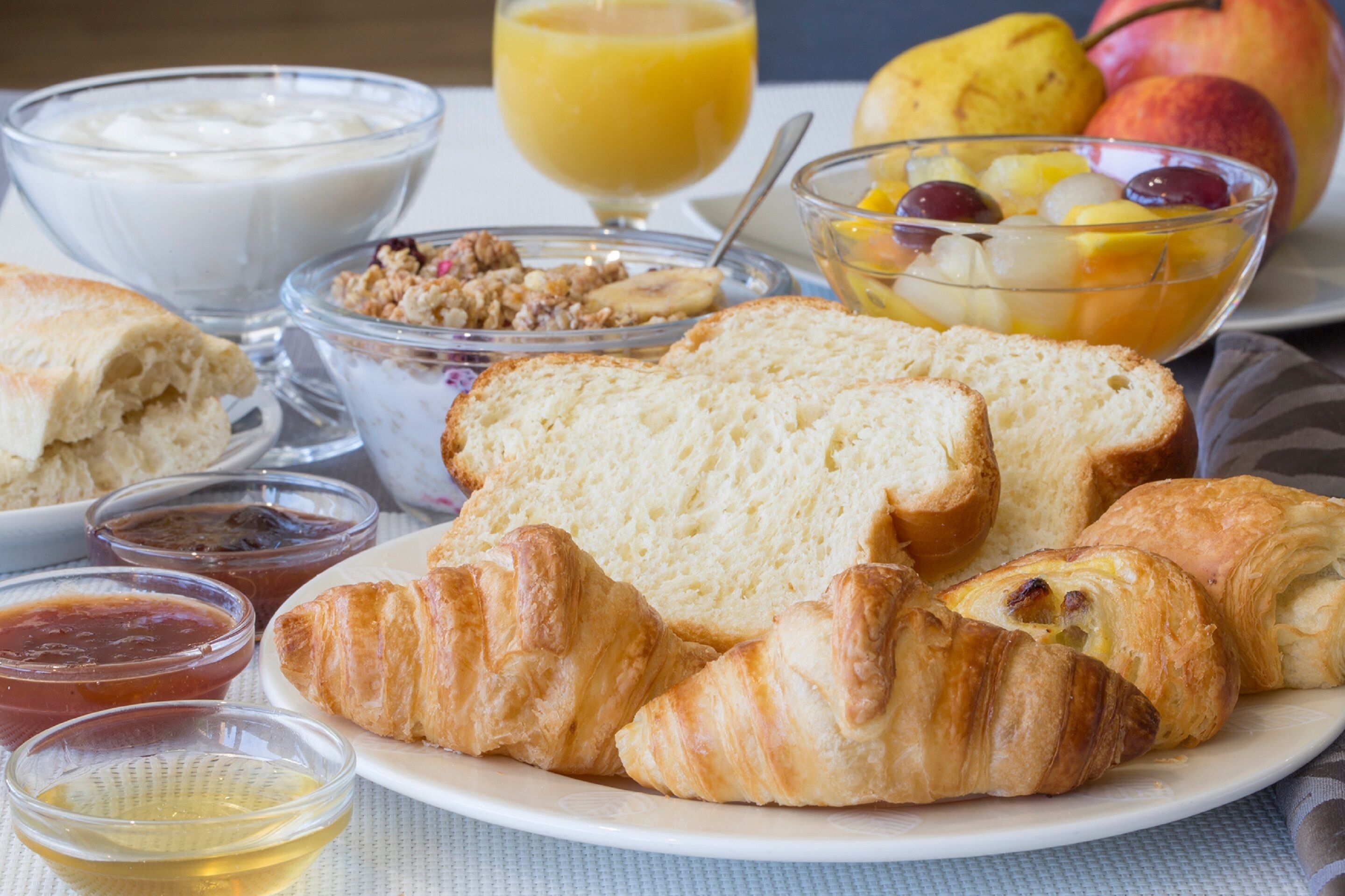 A breakfast plate with croissants, bread, and a bowl of fruit.