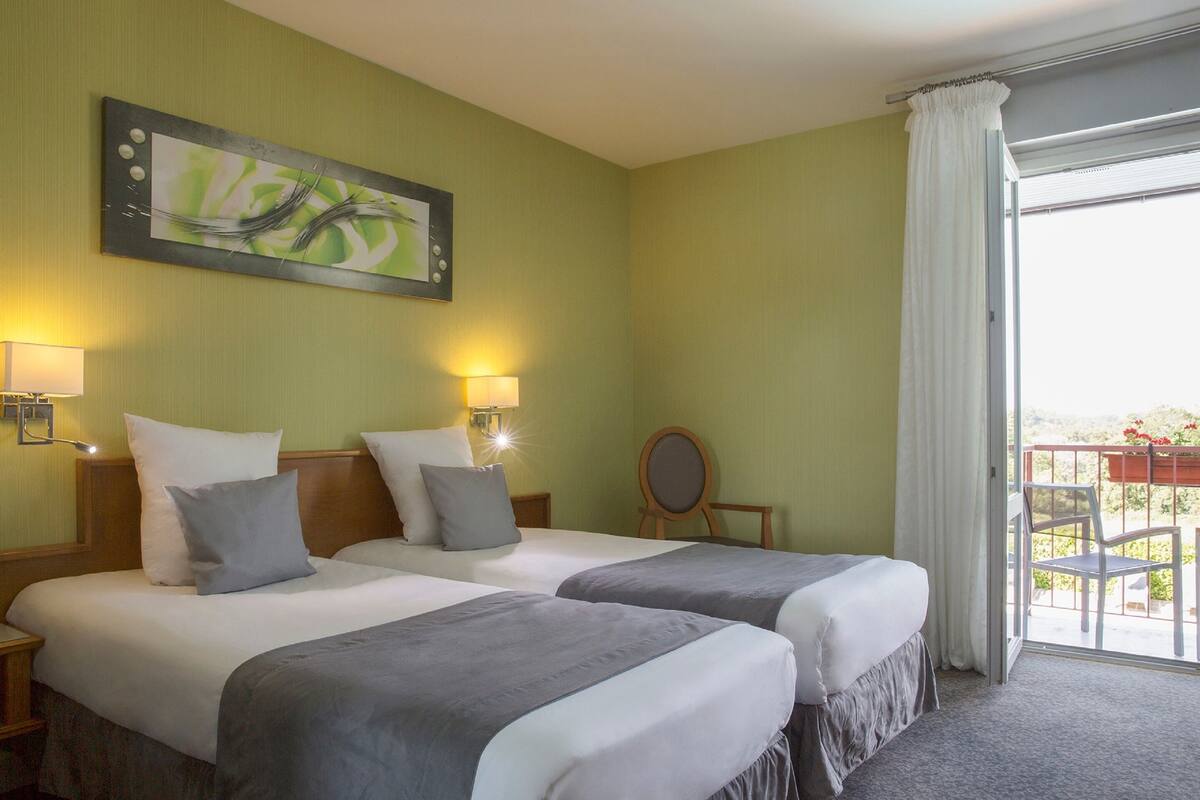 A hotel room with two beds, a painting on the wall, and a balcony with a view.