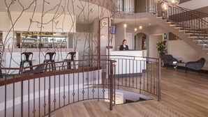 A spacious lobby with a central bar area, a staircase, and seating arrangements.
