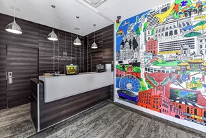 Zona de recepción de un hotel de diseño moderno, con mostrador de recepción, lámparas colgantes y un gran mural con vistas a la ciudad.