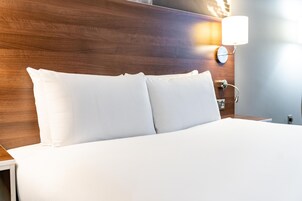 A neatly made bed with white linens in a hotel room.