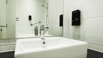 Un baño moderno con un lavamanos grande blanco, un cabezal de ducha de mano y un panel de control en la pared.