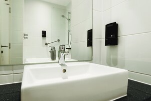 A modern bathroom with a large white sink, a handheld showerhead, and a wall-mounted control panel.