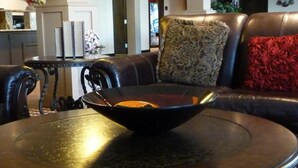 Un salon avec un canapé en cuir, une table ronde sur laquelle se trouve un saladier, et un coussin à motifs.