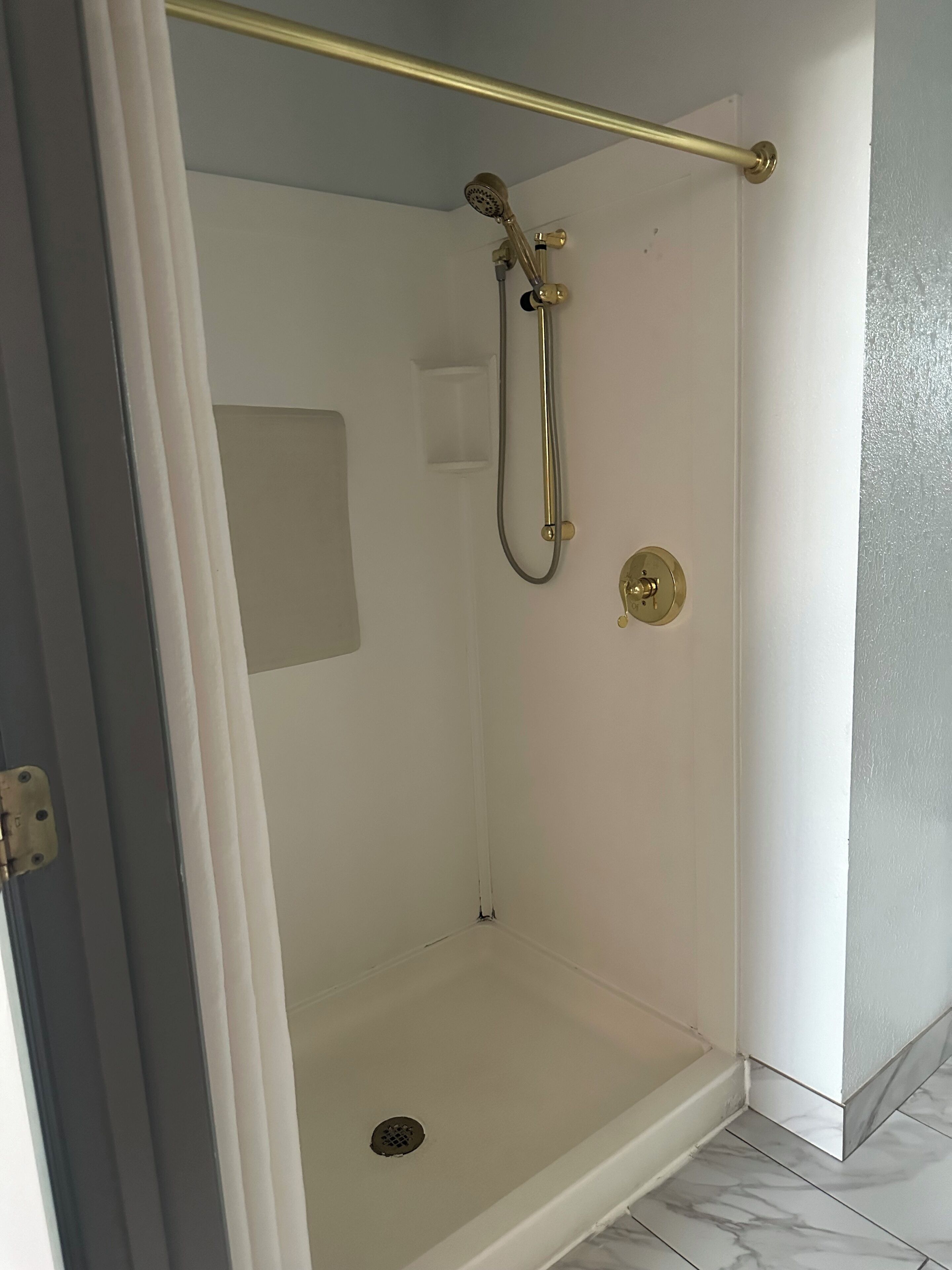 A walk-in shower with a glass door, a gold showerhead, and a white tiled floor.