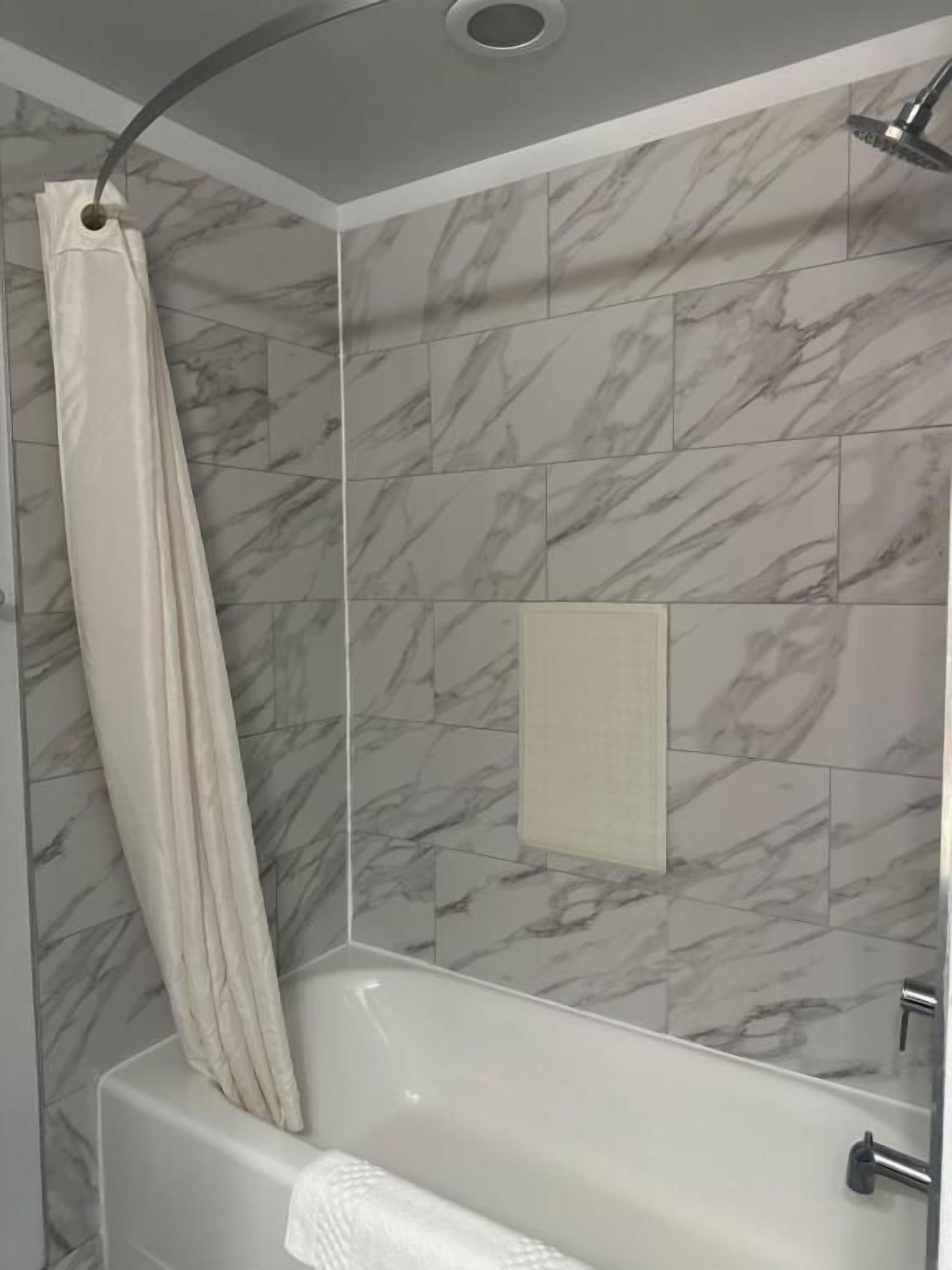 A bathroom with a bathtub, a shower curtain, and marble-patterned tiles.