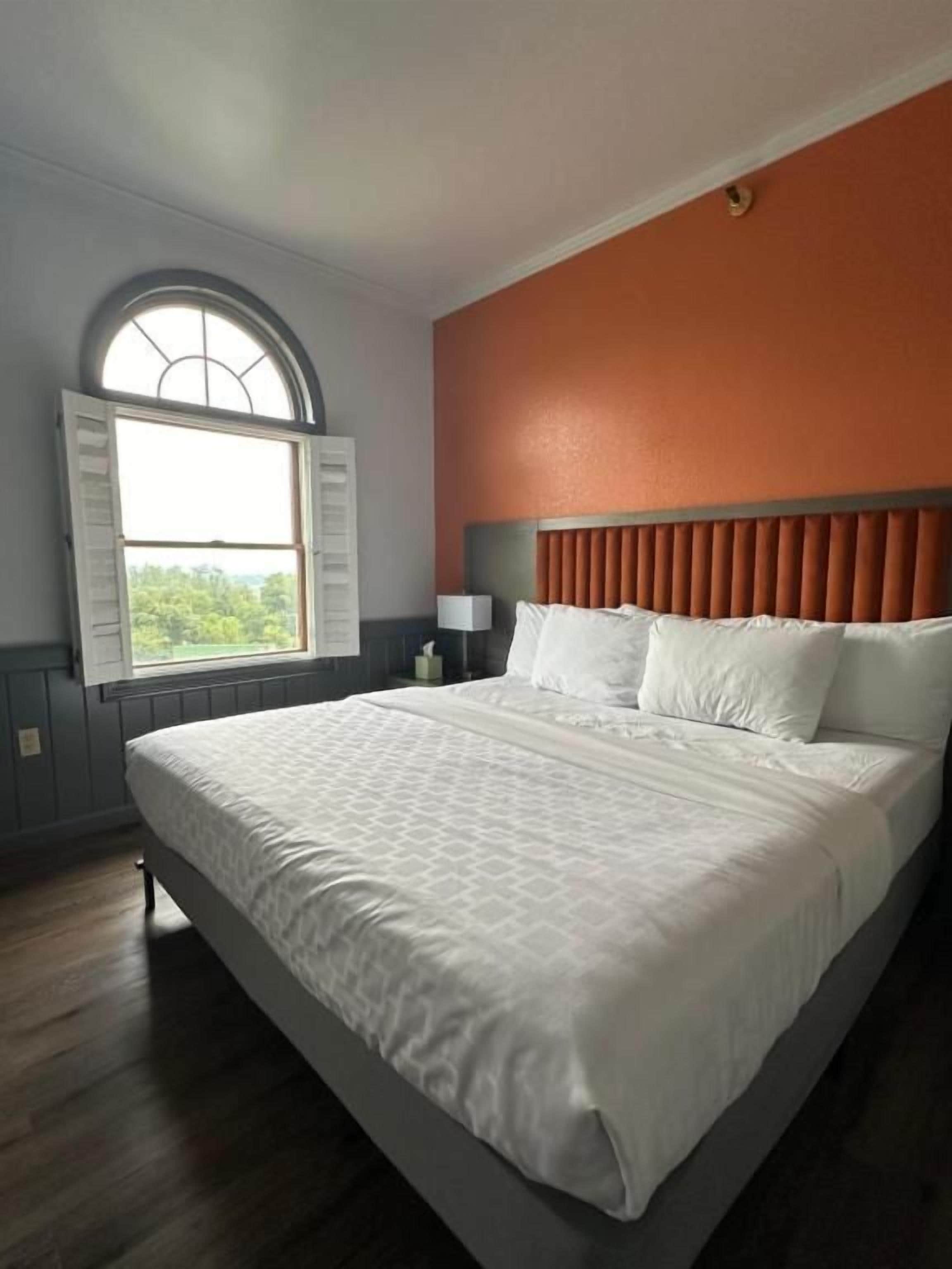 A hotel room with a large bed, a window with shutters, a nightstand, and a wall-mounted lamp.