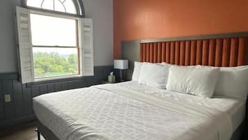 A hotel room with a large bed, a window with shutters, a nightstand, and a wall-mounted lamp.