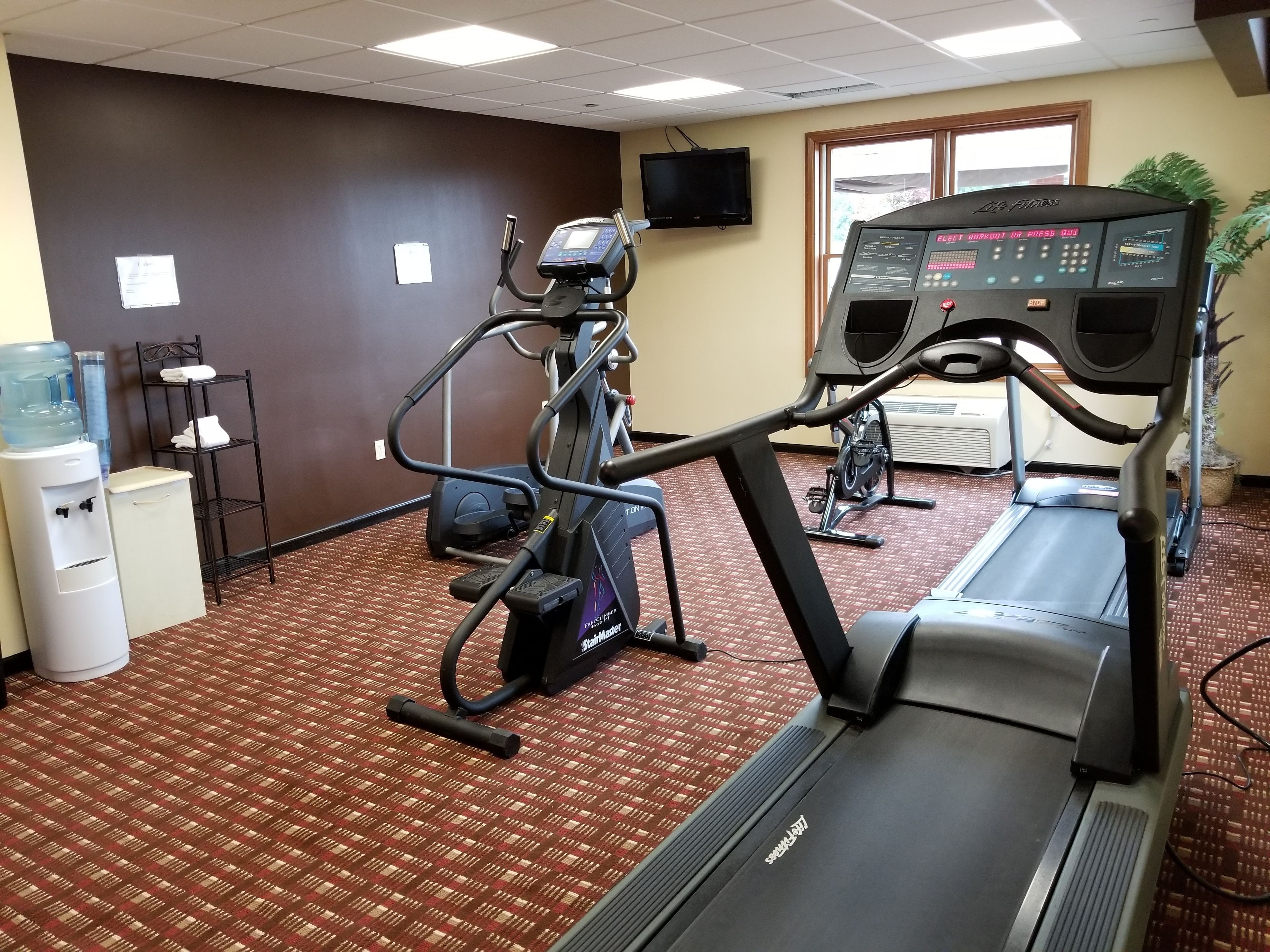A gym with treadmills, elliptical machines, and a water cooler.