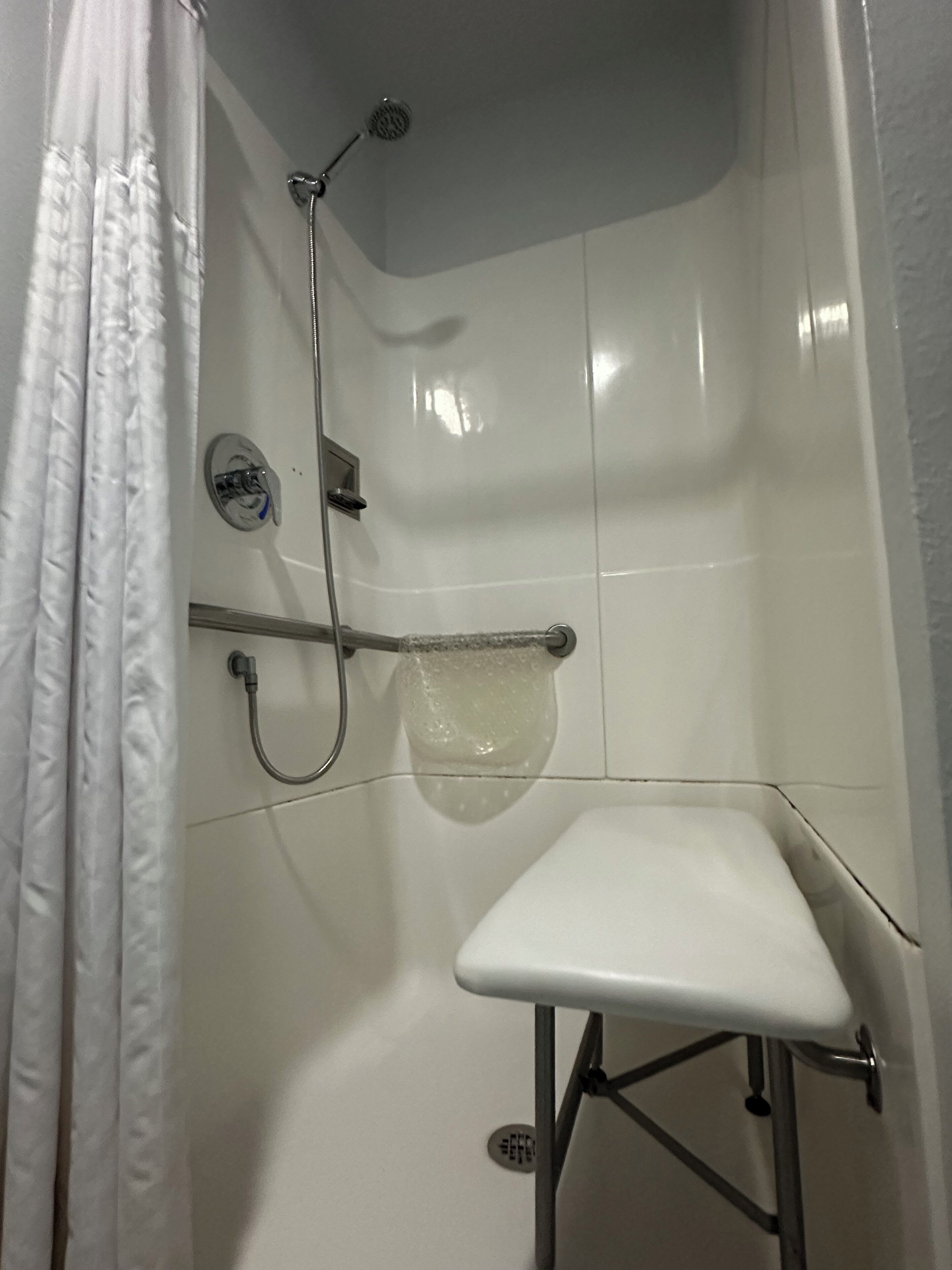 A small, enclosed shower area with a white seat, a handheld showerhead, and a handheld shower attachment.
