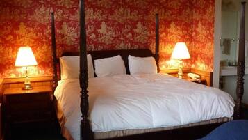 A four-poster bed with white linens, two bedside tables with lamps, and a floral wallpaper pattern.