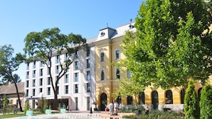 Un hôtel à la façade jaune, doté de nombreuses fenêtres et d’une cour intérieure agrémentée de plantes en pot et d’un banc.