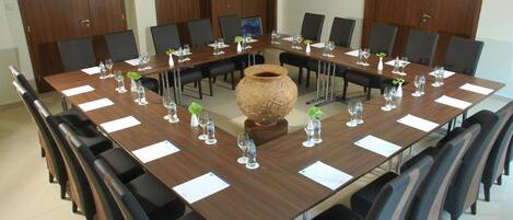 Un salón de conferencias con una larga mesa, sillas y un gran jarrón como centro de mesa.