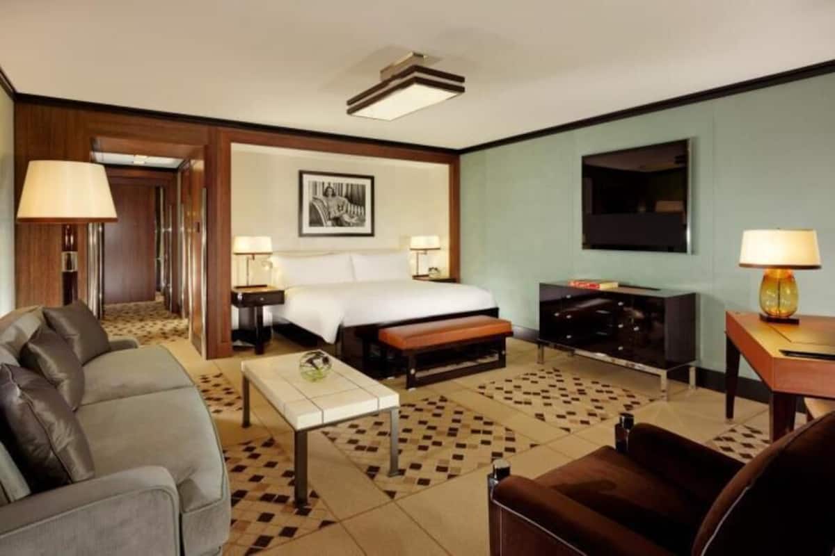 A hotel room with a bed, sofa, coffee table, TV, and a desk with a lamp.