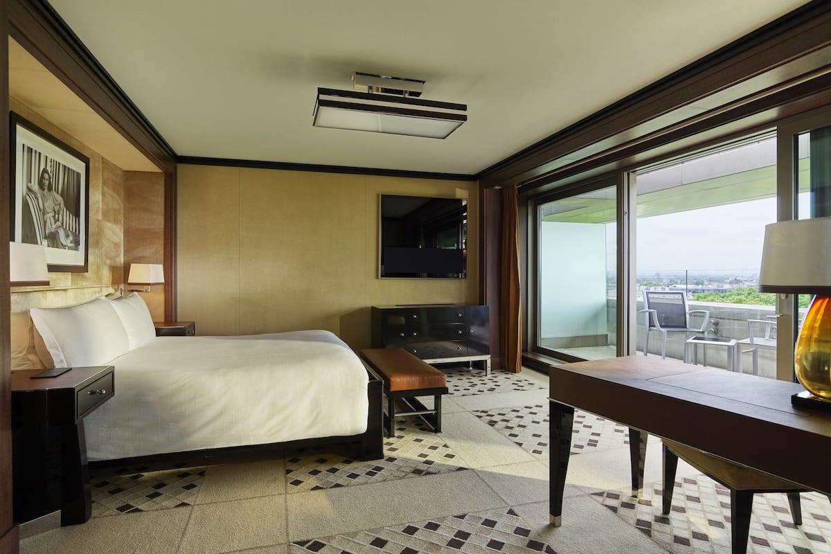 A hotel room with a bed, a desk, a chair, a TV, and a balcony with a view.