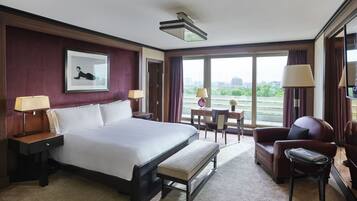 Habitación de hotel con una cama grande, un escritorio, una silla y vistas de la ciudad a través de amplias ventanas.