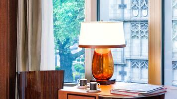 Une chambre d’hôtel avec un bureau en bois, une lampe, une chaise et une vue sur un immeuble par la fenêtre.