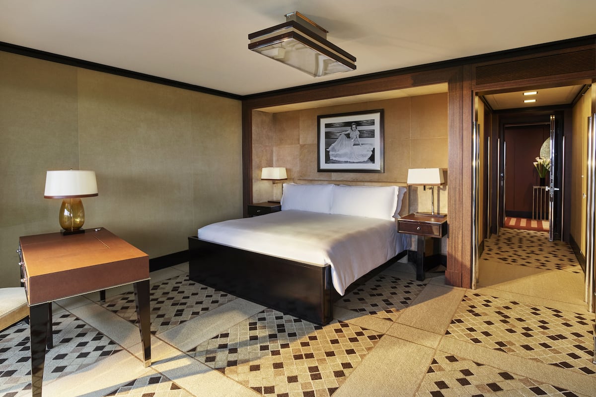A hotel room with a bed, two bedside tables with lamps, a framed picture on the wall, and a patterned floor.
