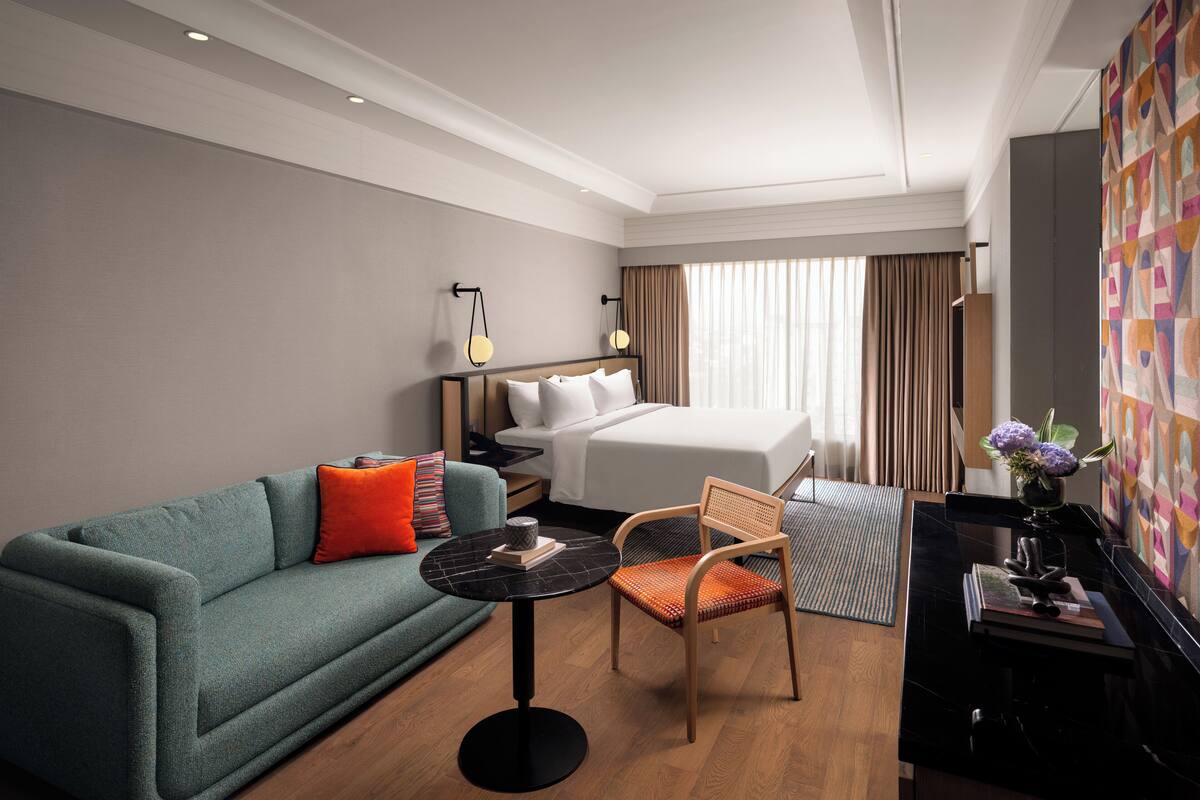 Una habitación de hotel con una cama, un sofá, una silla, una mesita y un escritorio con una lámpara.